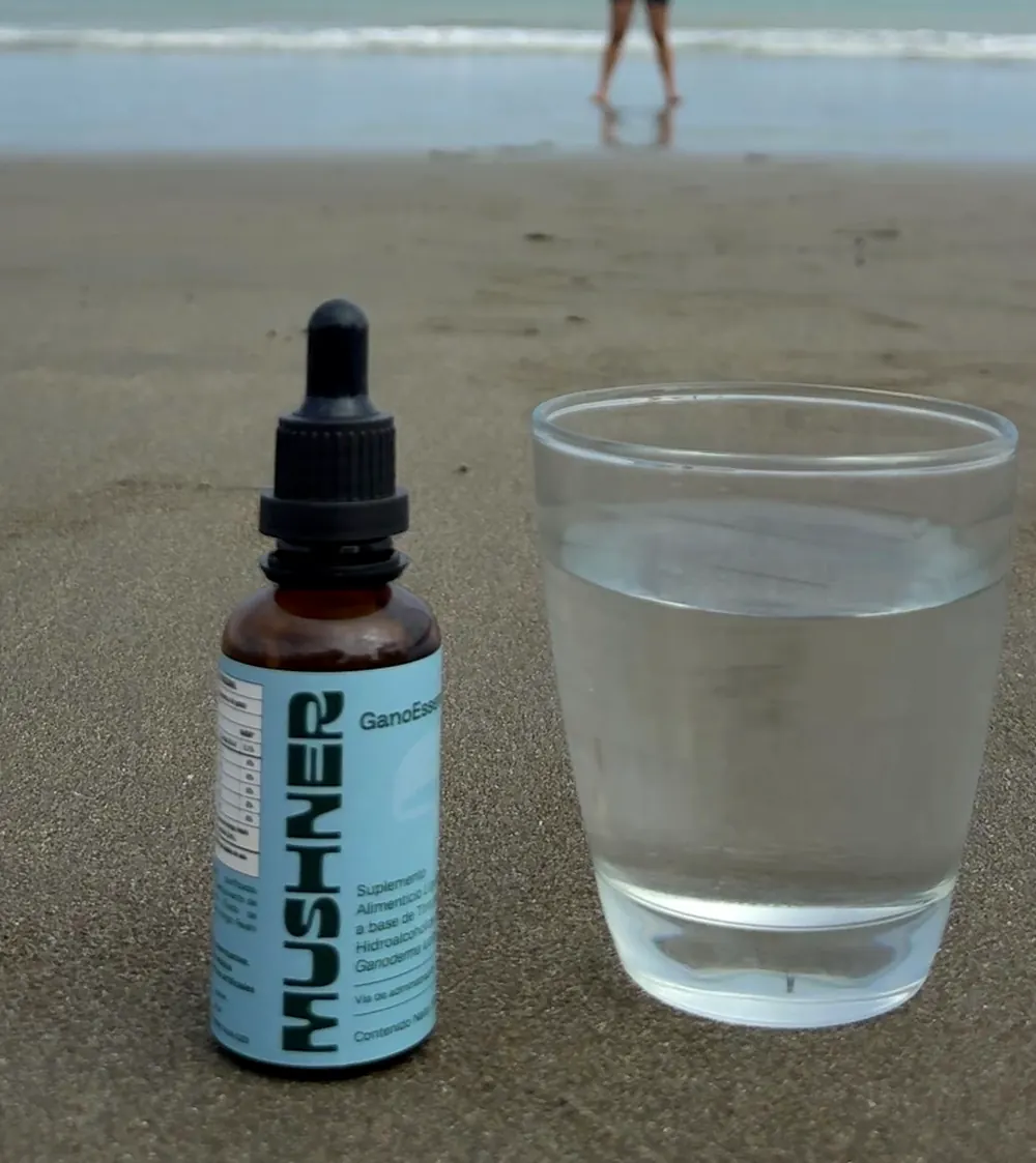 Frasco gotero ámbar de GanoEssence junto a un vaso de agua en la playa